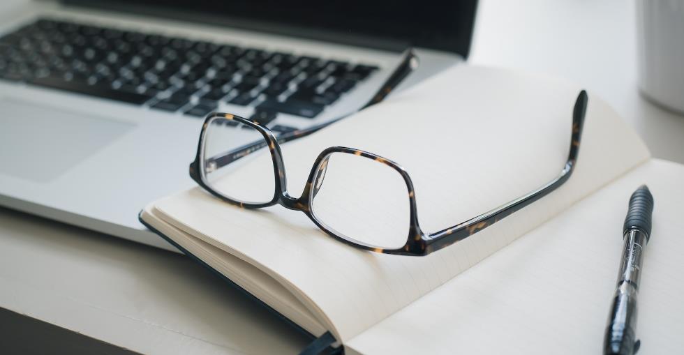 Glasses laying on a notebook with a pen