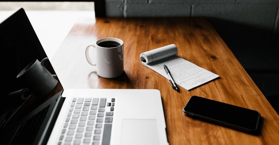 Laptop, pen and pad with a cup of coffee on a table