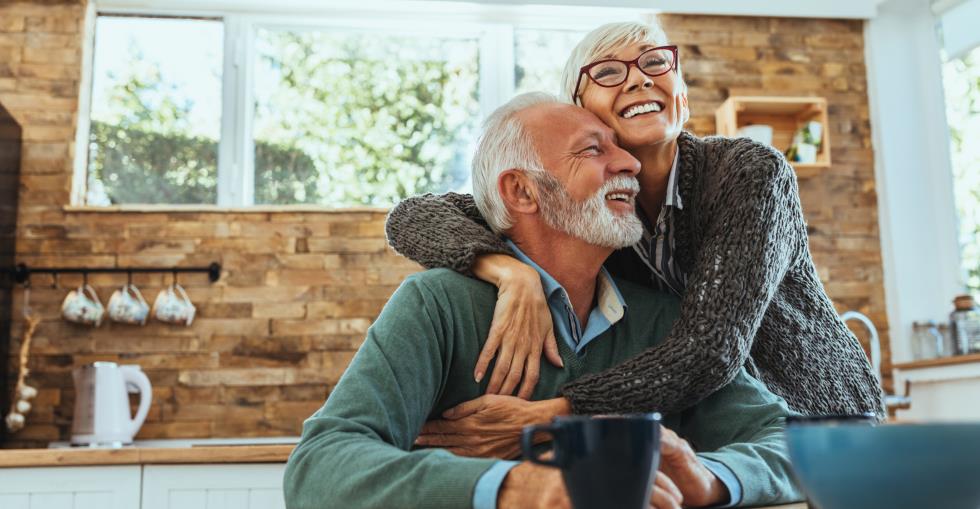 Mature couple hugging and smiling while planning retirement documents