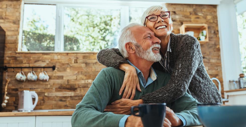 Mature couple hugging and smiling while planning retirement documents