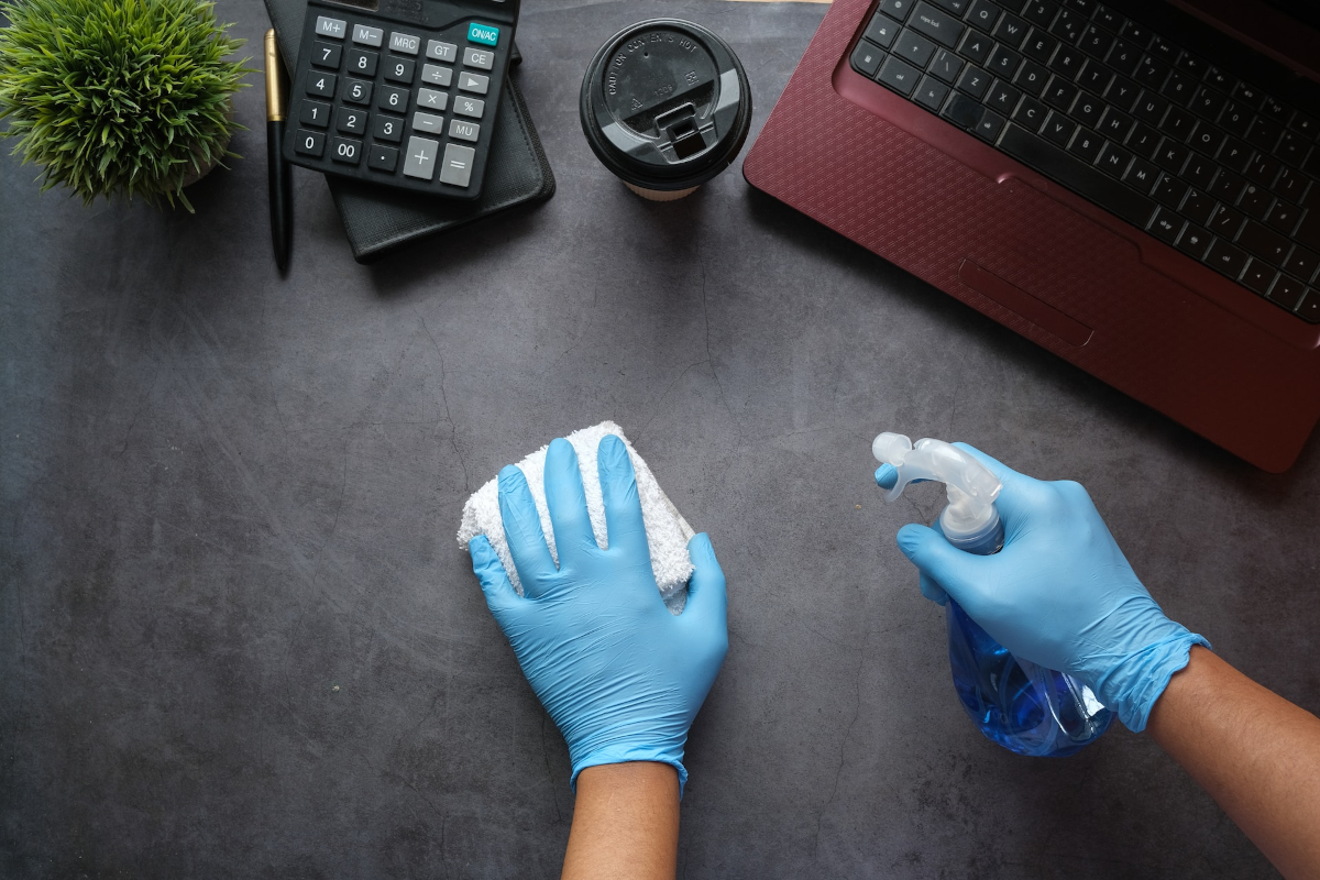 Someone cleaning an office desk with disinfectant
